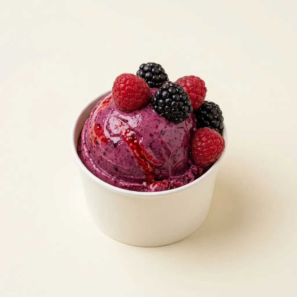Tarrina con una bola de gelato de frutos del bosque magenta oscuro con trozos de baya, sobre fondo crema.
